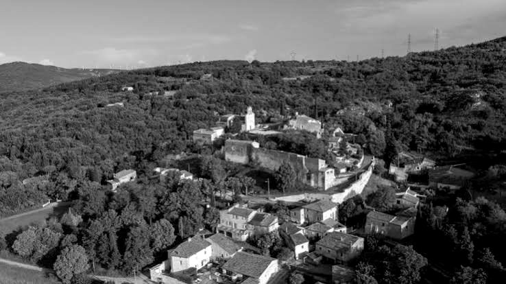 Le vieux village perché et ses remparts au milieu des collines boisées
